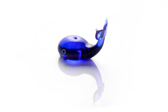 Wonderful figure of a blue whale made of glass photographed on the lumen.Isolated toy on white background.The view from the side.