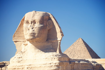 Close-up of the crumbling face of the Great Sphinx of Giza standing tall with the Great Pyramid in...