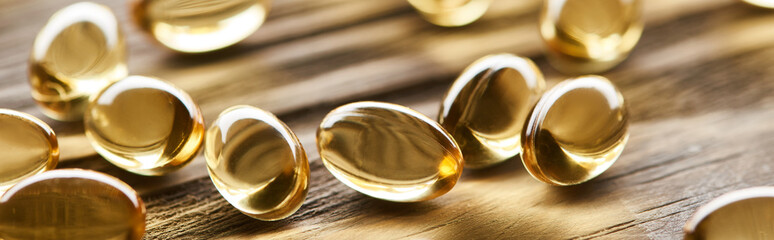 close up view of golden fish oil capsules scattered on wooden table, panoramic shot