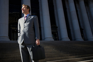 Confident lawyer businessman standing on dark steps with grand courthouse columns in the background