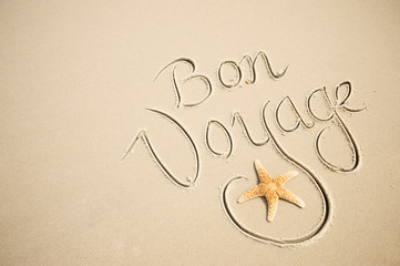 Bon Voyage message handwritten with a calligraphy script on a smooth sand beach with a starfish...