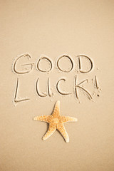 Good Luck! message handwritten on the beach with lucky starfish on smooth sand copy space