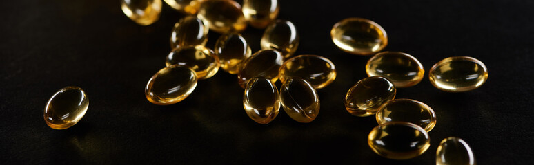 golden fish oil capsules scattered isolated on black, panoramic shot