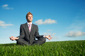Calm businessman sitting with eyes closed meditating in a seated yoga pose outdoors in fresh green meadow - obrazy, fototapety, plakaty