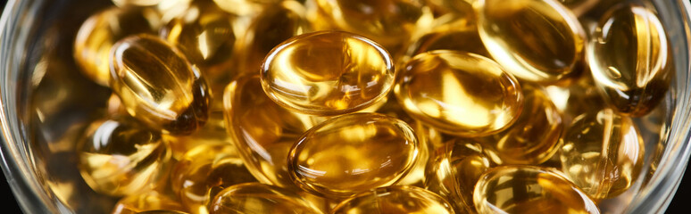 close up view of golden fish oil capsules in glass bowl, panoramic shot
