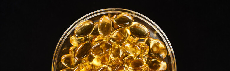 top view of golden fish oil capsules in glass bowl isolated on black, panoramic shot