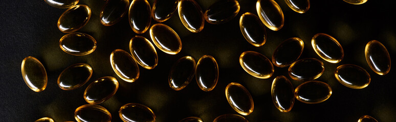 top view of golden fish oil capsules on black background in dark, panoramic shot