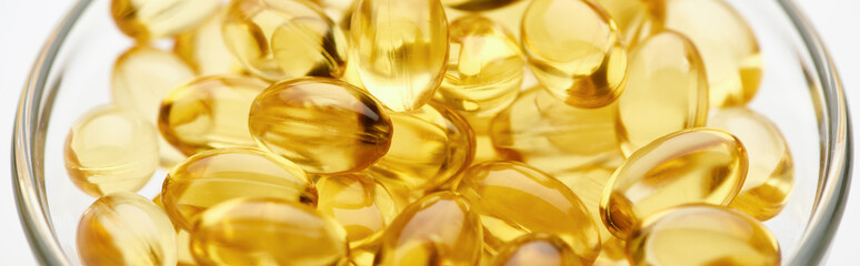 close up view of golden fish oil capsules in glass bowl on white background, panoramic shot