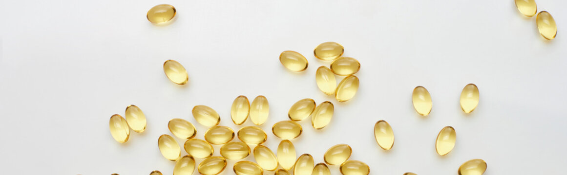 top view of golden fish oil capsules scattered on white background, panoramic shot