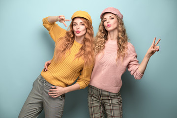 Two easy-going Woman happy smiling in Stylish fashion orange pink colored outfit. Beautiful young Girl in Trendy jumper, cap. Joyful sister, friend, Creative fashionable friendship happiness concept