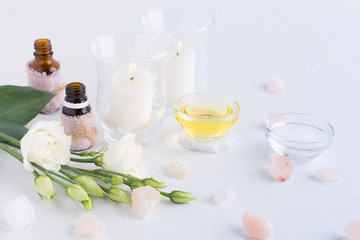 Spa composition with oils, sea salt, candles and a branch of white eustoma on a white background. Skin care concept