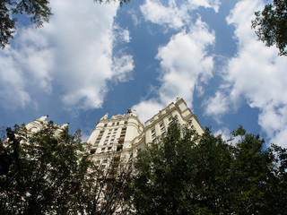 Multi-storey house among the trees, against the background of clouds and blue sky. Bottom view. Urban architecture in art Deco style.