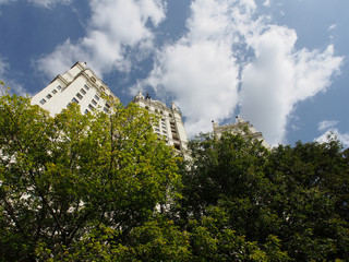 Multi-storey house among the trees, against the background of clouds and blue sky. Bottom view. Urban architecture in art Deco style.