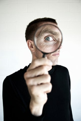 Man in black shirt looking with wide eye through a magnifying glass