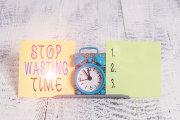 Writing note showing Stop Wasting Time. Business concept for Organizing Management Schedule lets do it Start Now Mini blue alarm clock standing above buffer wire between two paper