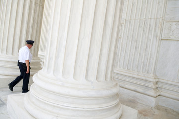 Unrecognizable security officer walking between classical fluted white marble columns and bases at the US Supreme Court building in Washington DC