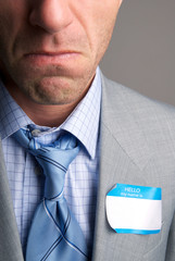Businessman with a sad expression on his face wearing a blank Hello My Name Is tag on the lapel of his suit