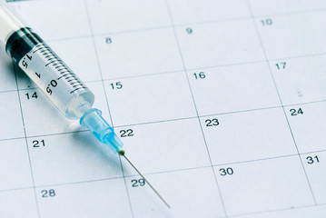Medical syringe on calendar background