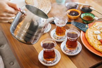 Pouring tea from tea pot to glass. Breakfast preparation concept. Traditional Turkish brewed tea drink in morning also as known 