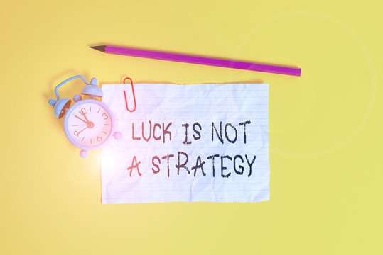 Conceptual hand writing showing Luck Is Not A Strategy. Concept meaning it is not being Lucky when planned intentionally Metal alarm clock ccrushed sheet pencil colored background