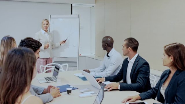 Confident mature businesswoman presenting new business project to coworkers in modern office