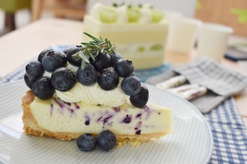 Slice of blueberry cheese pie on white plate with rosemary on top, selective focus.