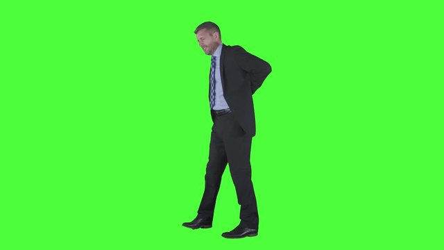 Caucasian businessman having back pain and walking back and forth in the studio. Sick worker concept. Shot in 4k resolution with green screen background