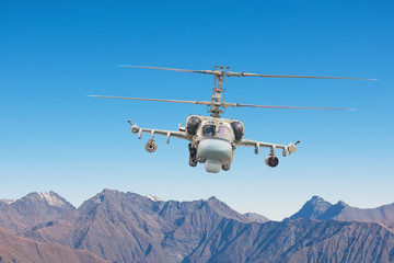 Military helicopter with armament flies on tops of mountains.