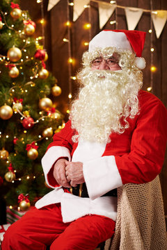 Santa Claus portrait, sitting indoor near decorated xmas tree with lights - Merry Christmas and Happy Holidays!