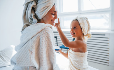 Using cream to clear skin. Young mother with her daugher have beauty day indoors in white room