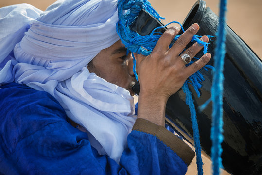 Moroccan man dressed with turban drinks water from a well in the Sahara desert.