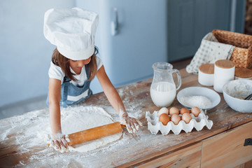 Cute kid in white chef uniform preparing food on the kitchen