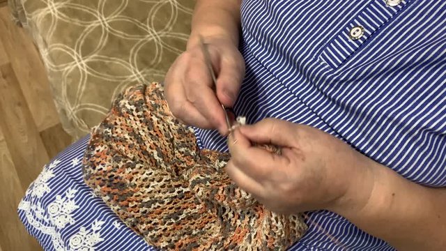Crochet. Needlework. Close-up of the hands of an elderly woman knitting a beautiful openwork cape.