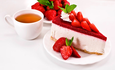 Piece of cheesecake with fresh strawberries, mint and cup of tea on a white background