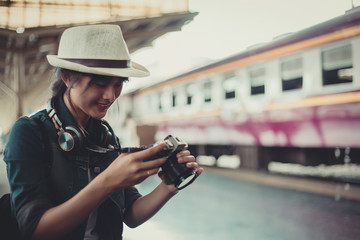Commuter traveler woman looking down at camera waiting train in railway station - Cute girl caucasian guy sitting on platform using cam with locomotive background - Soft desaturated vintage filter