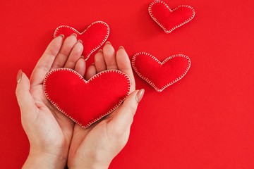 Romantic greeting card. Top view of handmade felt heart in woman hands over red background. Copy space.