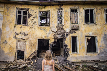 A woman in a dress stands in the background of an old abandoned dilapidated house
