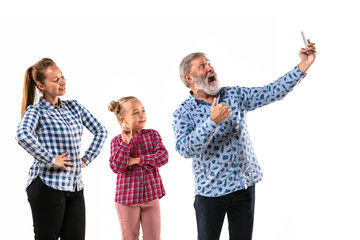 Happy family with child looks happy and posing isolated on white studio background. Concept of human emotions, facial expression, good relations. Maling selfie. Grandpa, mother and daughter.