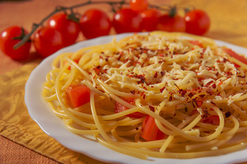 Italian Parmesan pasta on a white plate, sprinkled with spices and decorated with chili tomatoes