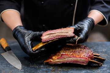 Grill restaurant kitchen. Closeup of chef hands in black cooking gloves holding smoked beef ribs.