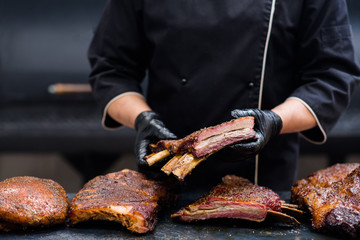 Catering service. Cropped shot of chef holding smoked beef ribs. Grilled meat on kitchen table.