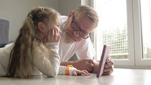 Intelligent grandfather showing his little granddaughter pictures in book, telling interesting facts and laughing together