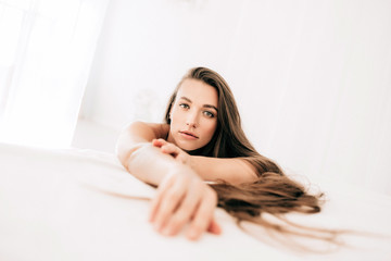 Fototapeta premium A young beautiful woman with long hair wakes up on the white bed at home, top view.