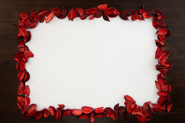 Flat lay Christmas copy space space with red petals bordering a white background and dark wood all around