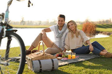 Happy young couple having picnic near lake on sunny day