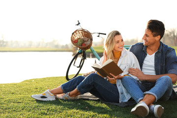 Happy young couple reading book while having picnic outdoors