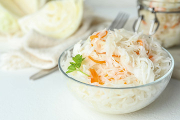 Glass bowl of tasty fermented cabbage on white table, closeup