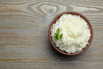 Tasty fermented cabbage with parsley on wooden table, top view. Space for text