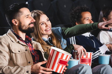 selective focus of woman pointing with finger and watching movie with multicultural friends in cinema