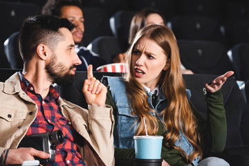 selective focus of man shooting with digital camera and showing shh gesture to angry woman in cinema